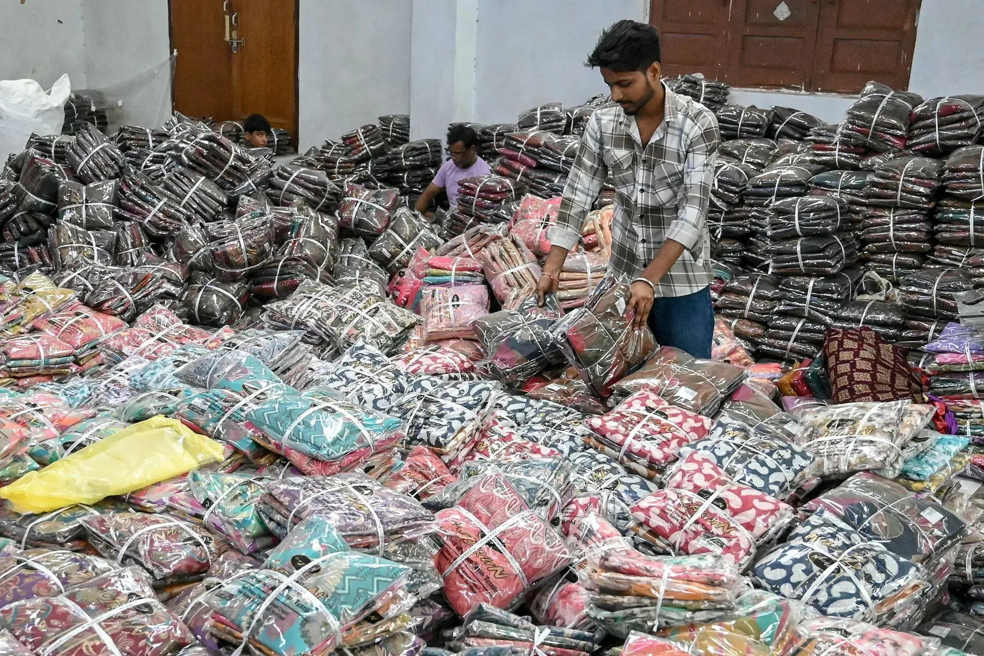 رجل يرتب أكياس الملابس الملونة في مستودع، مما يعكس تأثير الرسوم الجمركية الجديدة على التجارة مع الهند.