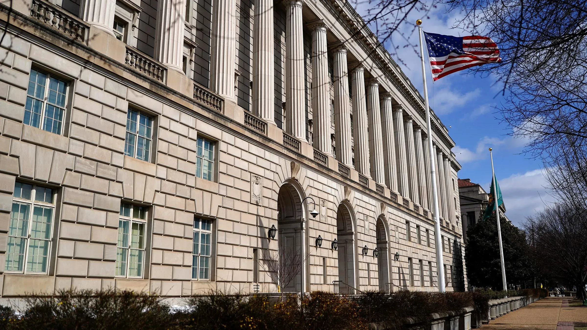 مبنى مصلحة الضرائب الأمريكية يظهر من زاوية، مع العلم الأمريكي يرفرف في المقدمة، ويعكس أهمية التعيينات الحكومية الحالية.