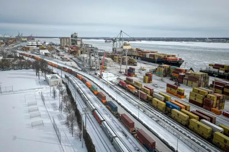 مشهد لميناء مزدحم بالحاويات والشاحنات، مع تساقط الثلوج، يعكس تأثير السياسات الاقتصادية لدونالد ترامب على التجارة الأمريكية.