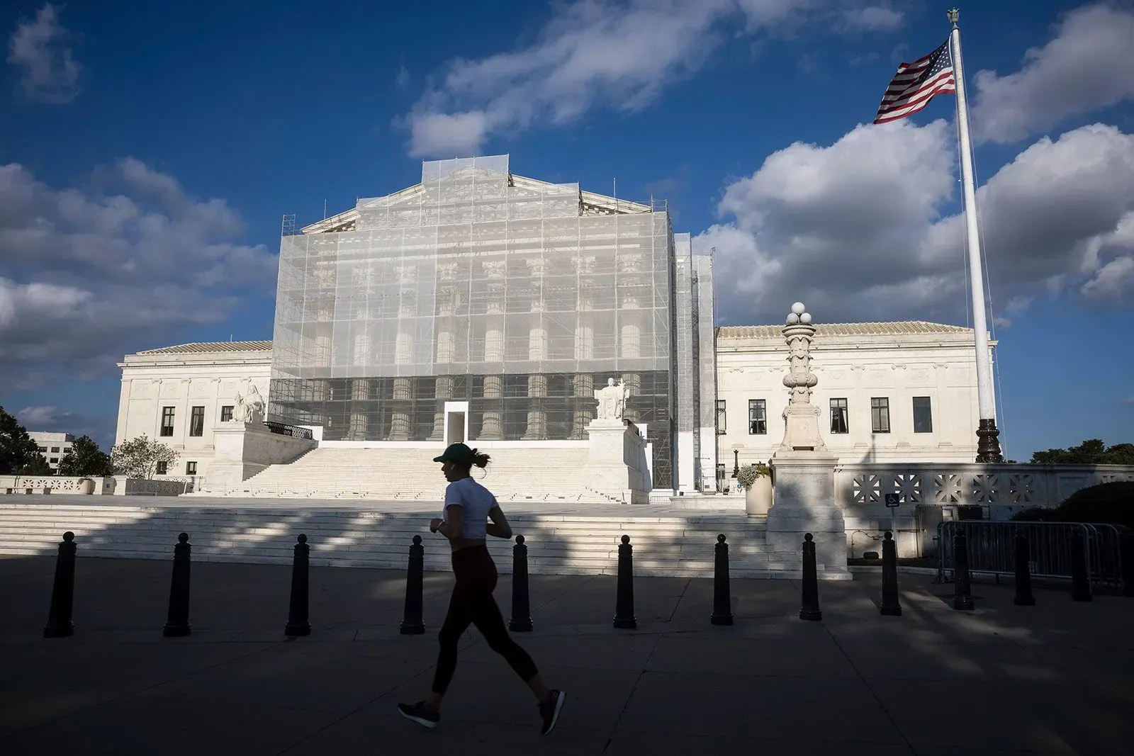 واجهة المحكمة العليا الأمريكية مغطاة بشبكة، مع شخص يجري في المقدمة، تعكس التوترات القانونية حول المساعدات الخارجية.