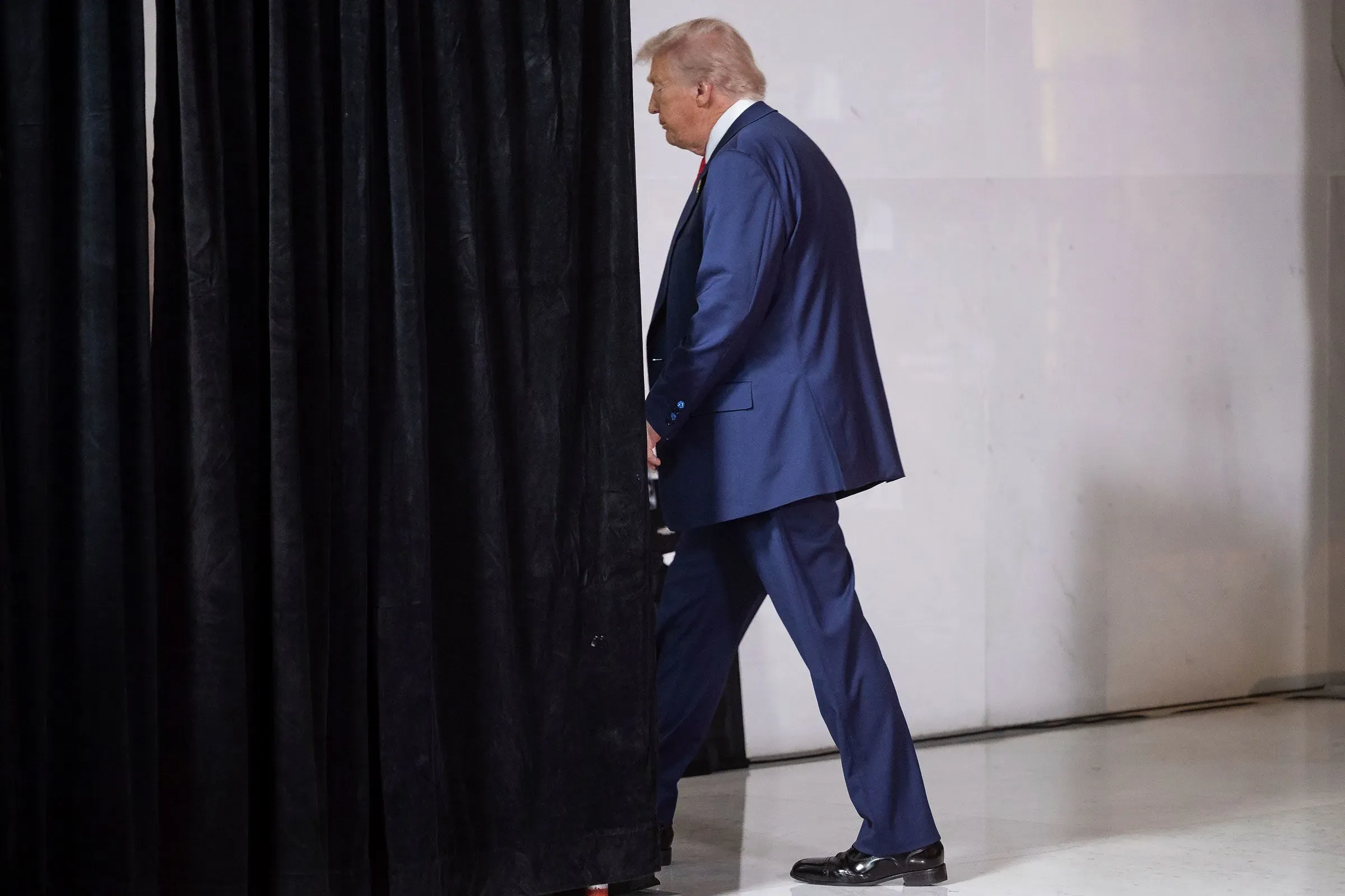 ترامب يغادر خلف ستارة سوداء، مرتديًا بدلة زرقاء، في سياق التوترات السياسية المتزايدة حول تحقيقاته ومواجهاته مع خصومه.
