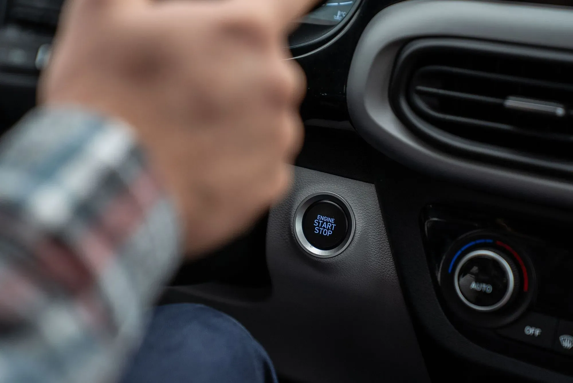زر تشغيل وإيقاف المحرك في سيارة حديثة، مع يد شخص تلمسه. الصورة تعكس التغييرات المحتملة في تقنيات السيارات بعد إلغاء لوائح انبعاثات السيارات.