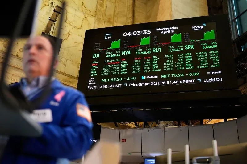 شاشة تعرض بيانات سوق الأسهم في بورصة نيويورك، مع ارتفاع مؤشرات داو جونز وستاندرد آند بورز 500، بينما يظهر تاجر في المقدمة.