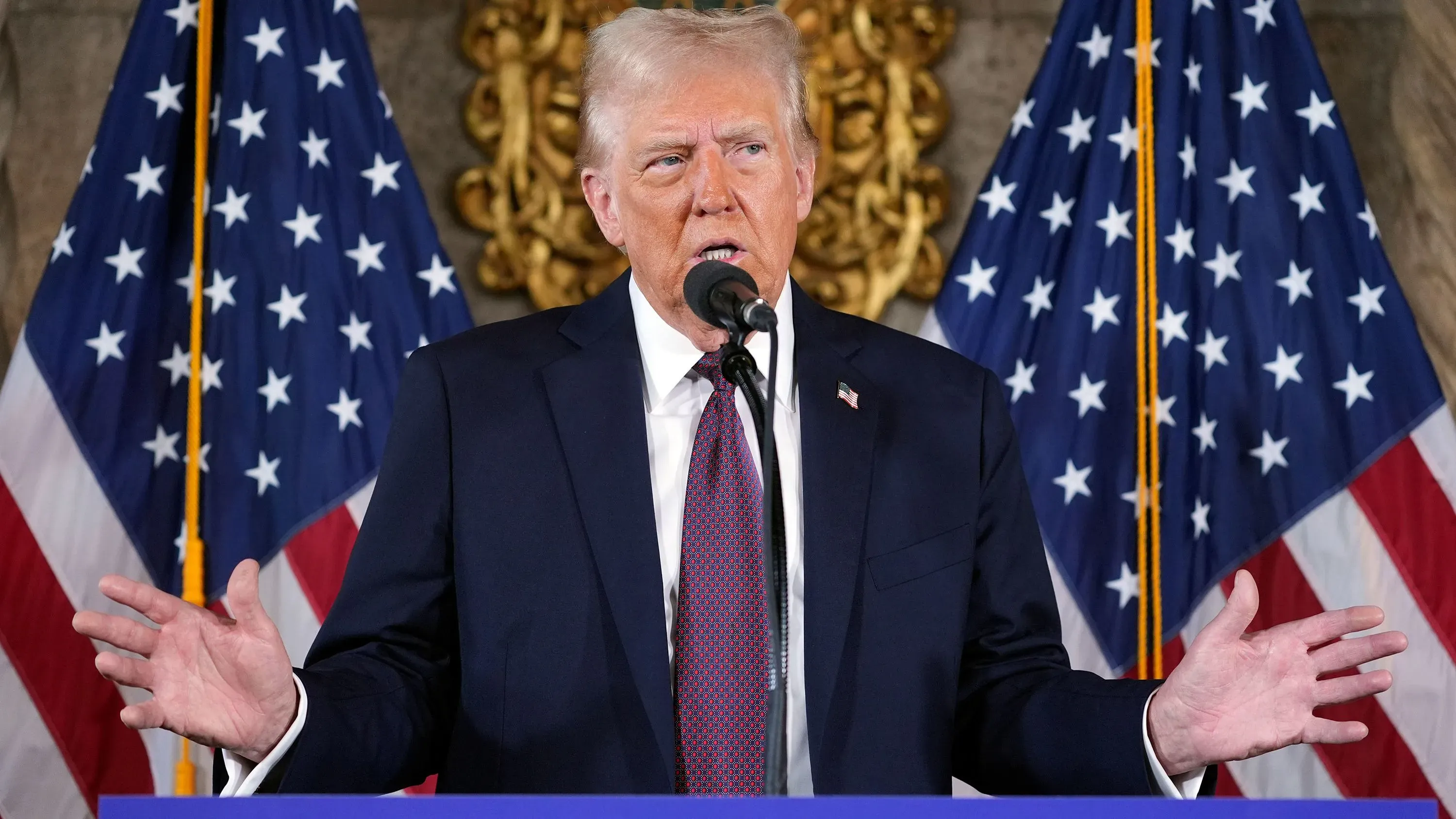 دونالد ترامب يتحدث أمام الصحفيين في مار-أ-لاجو، مع أعلام الولايات المتحدة خلفه، مستعرضًا أفكاره حول توسيع نفوذ أمريكا في نصف الكرة الغربي.