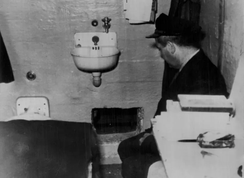 صورة تاريخية لزنزانة في سجن الكاتراز، تُظهر حارسًا ينظر إلى فتحة تهوية، مع تفاصيل بسيطة عن المرافق.