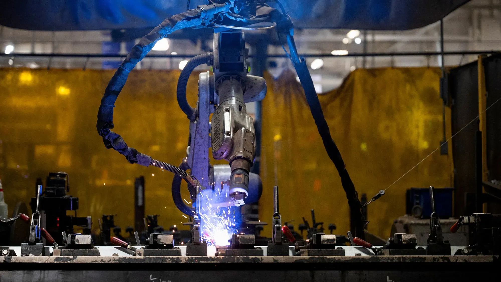 روبوت لحام يعمل في مصنع، مع شرارات تتطاير، يعكس التحول نحو الأتمتة في قطاع التصنيع الأمريكي.