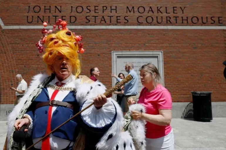 شخص يرتدي زيًا ملكيًا ملونًا، يقف أمام مبنى محكمة الولايات المتحدة، مع تجمع الناس حوله، مما يعكس أجواء الاحتجاجات.