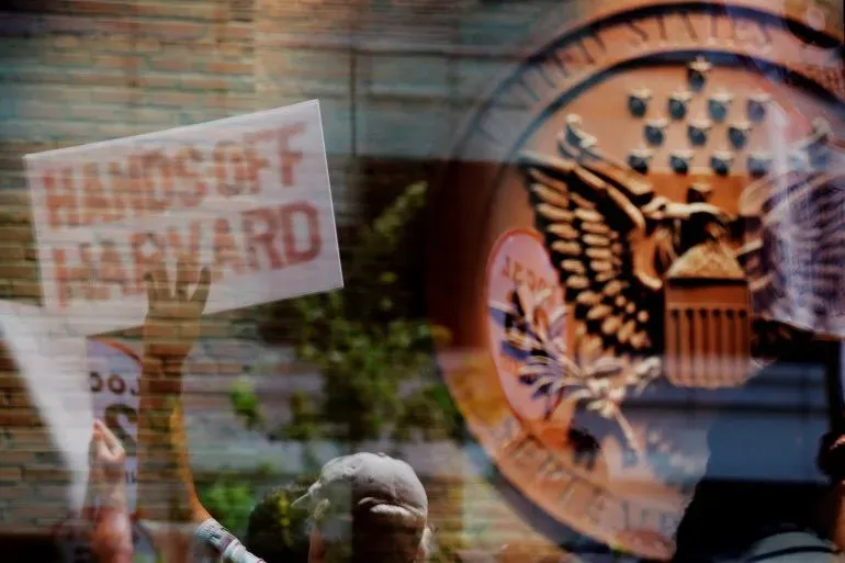 متظاهر يحمل لافتة مكتوب عليها "لا تلمس هارفارد" أمام شعار وزارة الخارجية الأمريكية، مع خلفية تعكس أجواء الاحتجاجات.