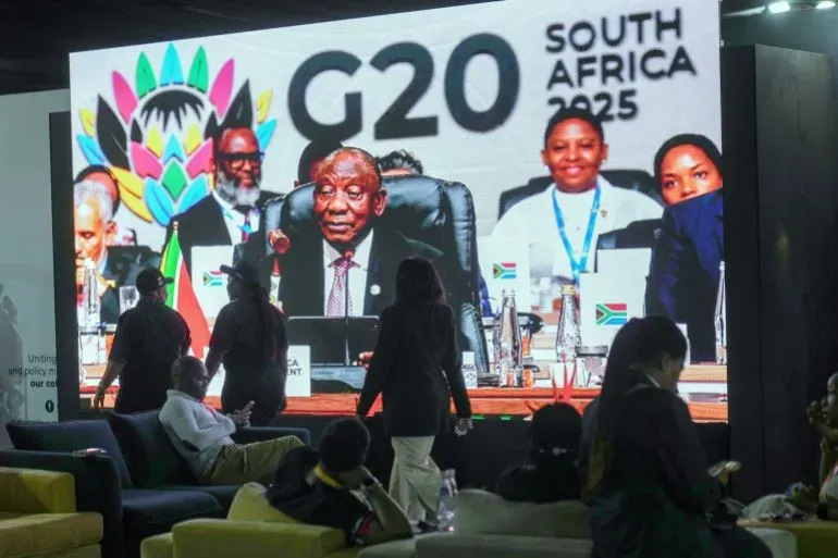 لقطة من قمة مجموعة العشرين في جنوب أفريقيا، تُظهر الرئيس سيريل رامافوزا يتحدث، مع وجود أعلام الدول المشاركة، وسط أجواء دبلوماسية.