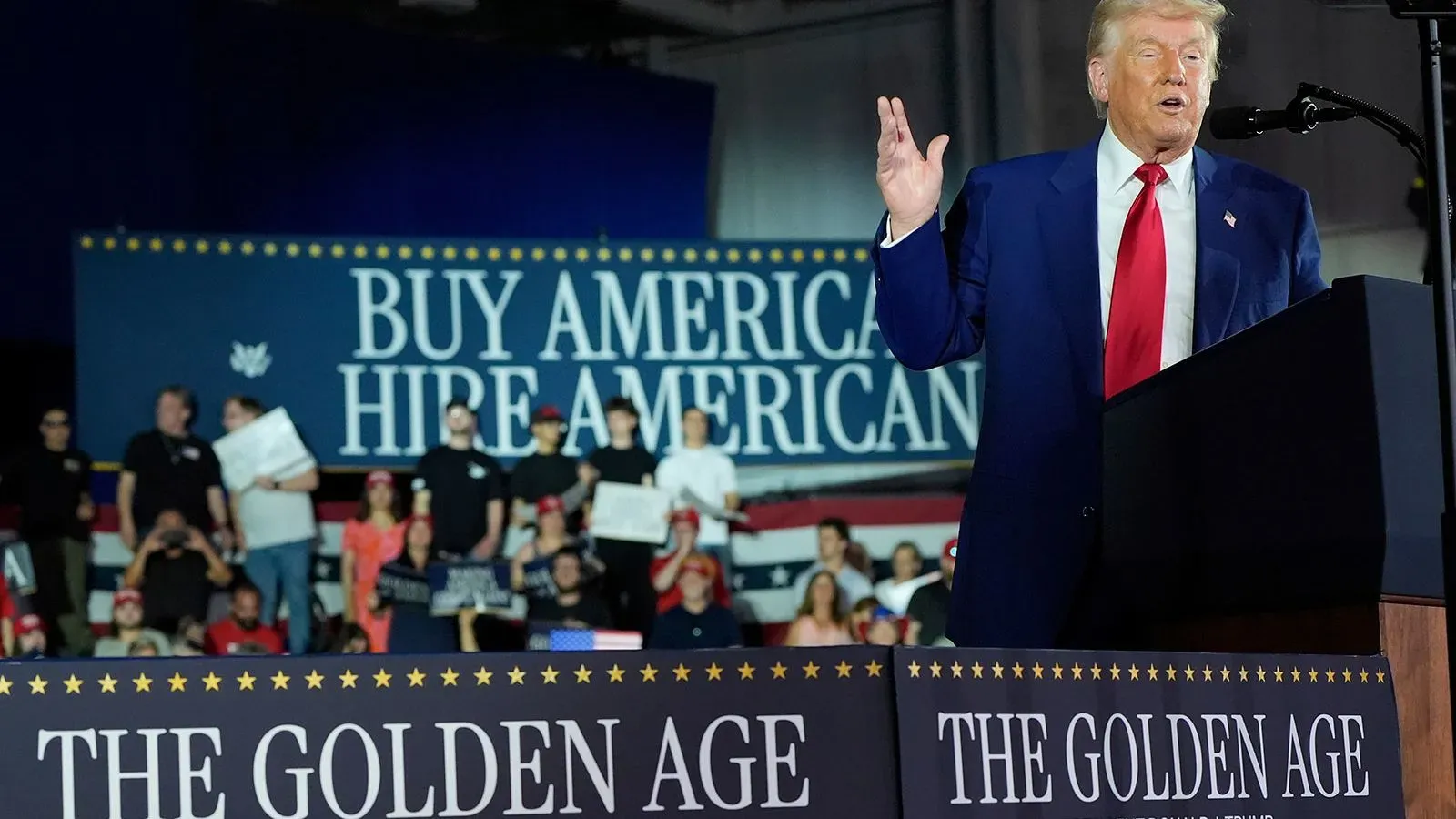 ترامب يلقي خطابًا أمام حشد من المؤيدين في ميشيغان، مع لافتات تدعو لشراء وتوظيف الأمريكيين، مع التركيز على "العصر الذهبي".