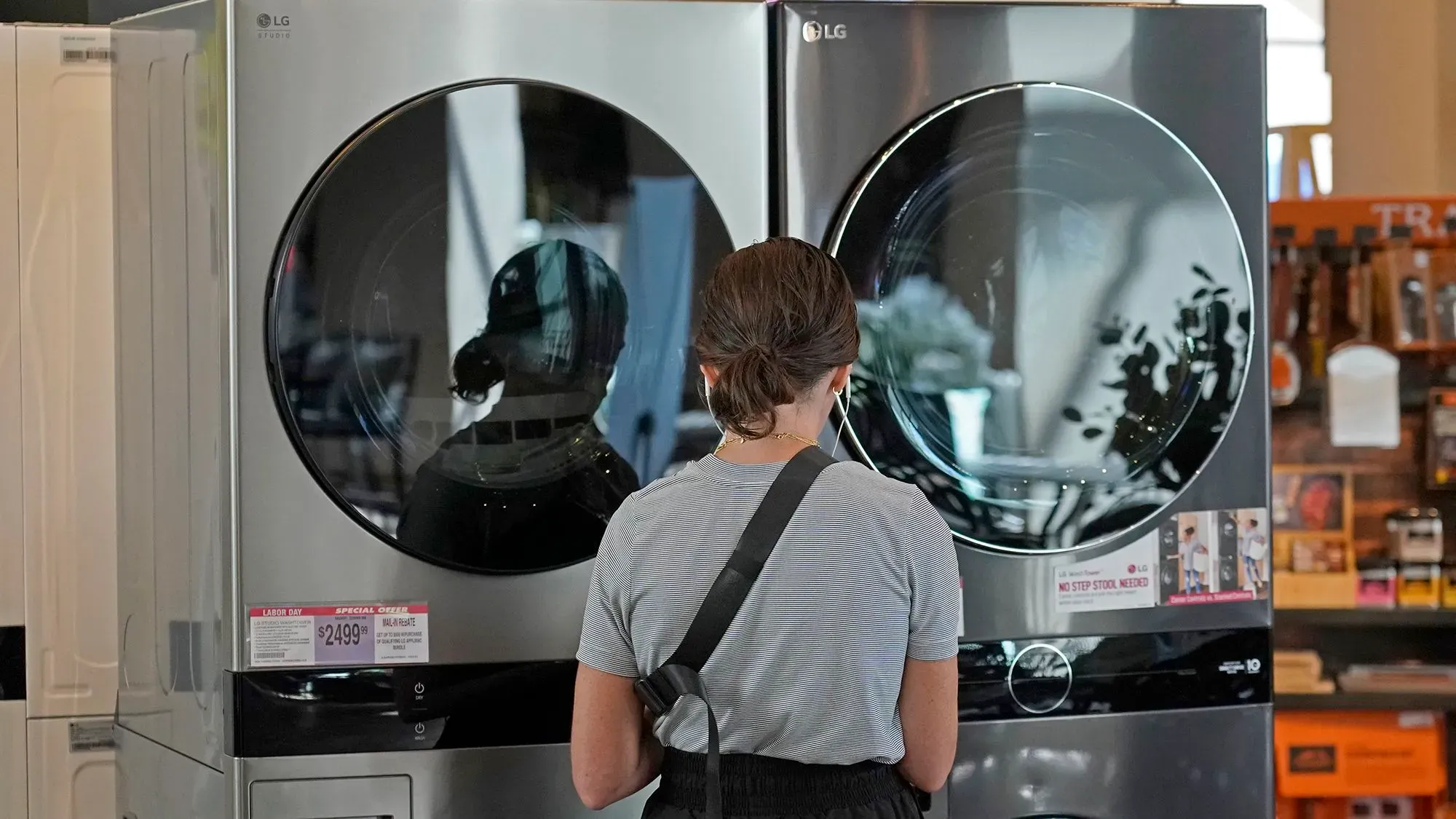 امرأة تتفقد غسالة ملابس وثلاجة في متجر للأجهزة، مع التركيز على تأثير التعريفات الجمركية على الأسعار.