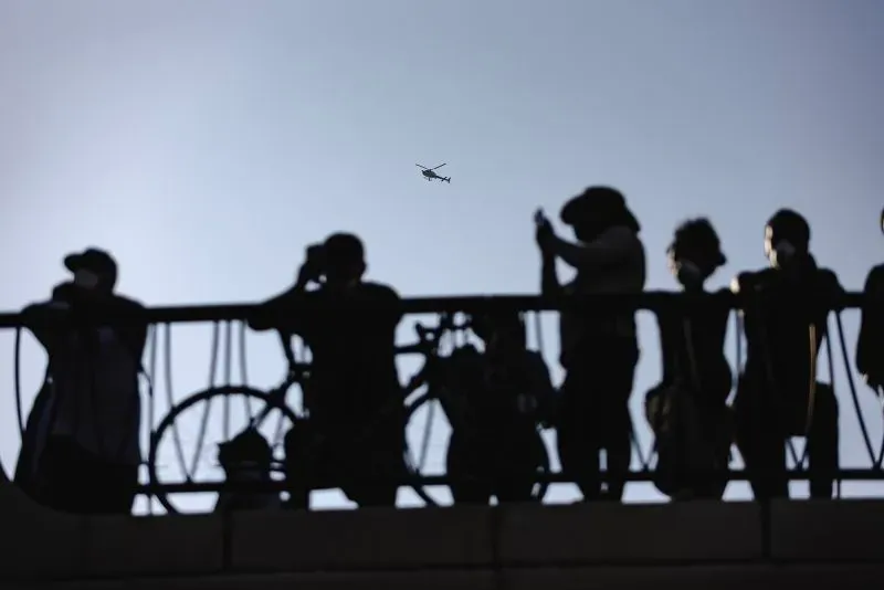 محتجون يراقبون مروحية تحلق فوقهم خلال الاحتجاجات في كاليفورنيا، حيث تصاعدت التوترات بعد مداهمات إدارة الهجرة.