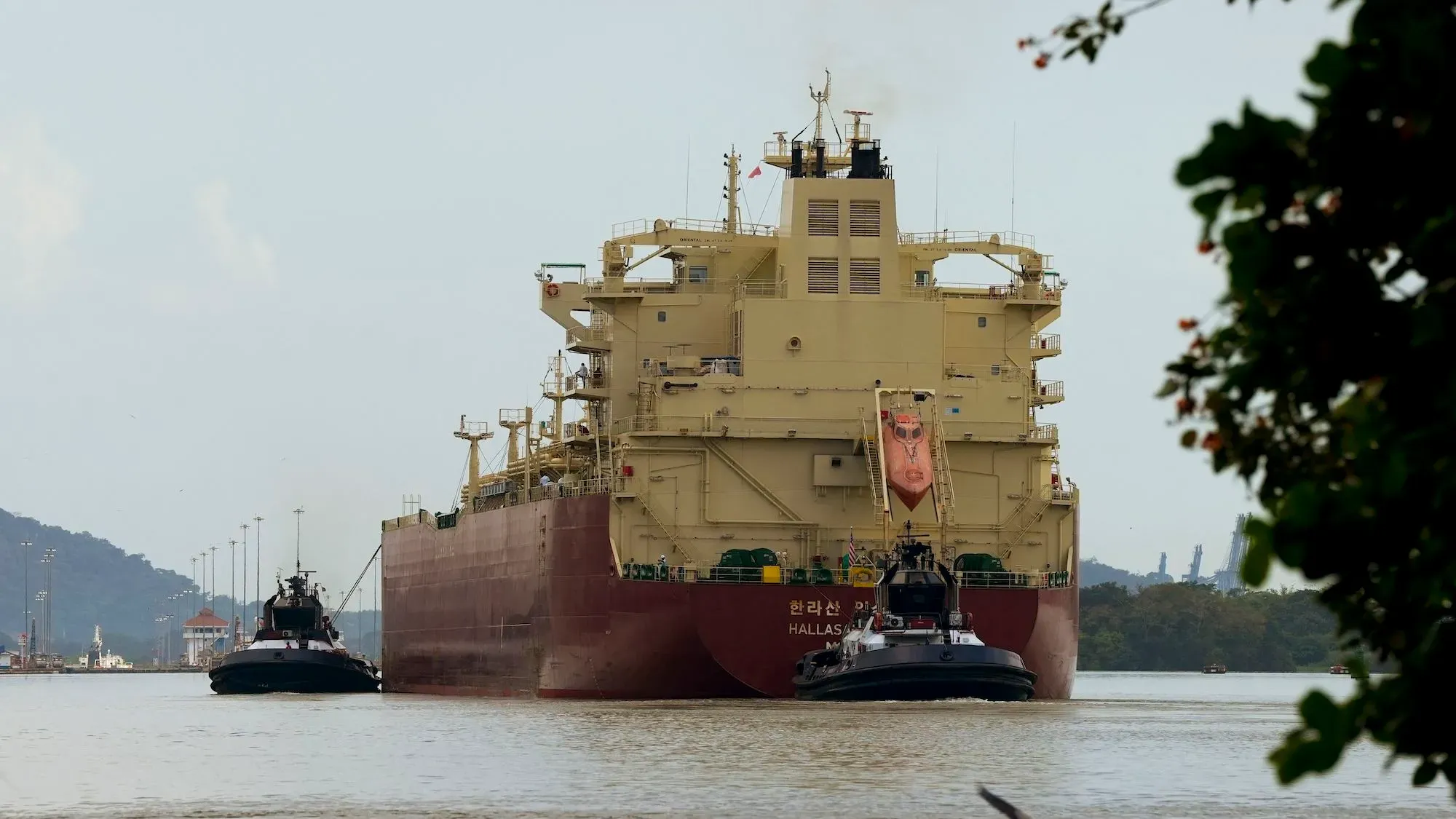 سفينة كبيرة تعبر قناة بنما، مع قوارب مساعدة تقترب منها، مما يعكس أهمية القناة في التجارة العالمية.