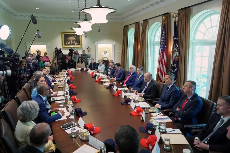 اجتماع مجلس الوزراء الأمريكي، حيث يجلس ترامب مع مستشارين ورجال أعمال، مع وجود كاميرات وإضاءة، في سياق مناقشة الاقتصاد والتجارة.