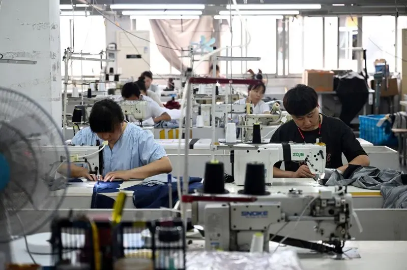 عمال في مصنع خياطة يقومون بتشغيل آلات الخياطة، مما يعكس تأثير الحرب التجارية بين الولايات المتحدة والصين على سلاسل التوريد.