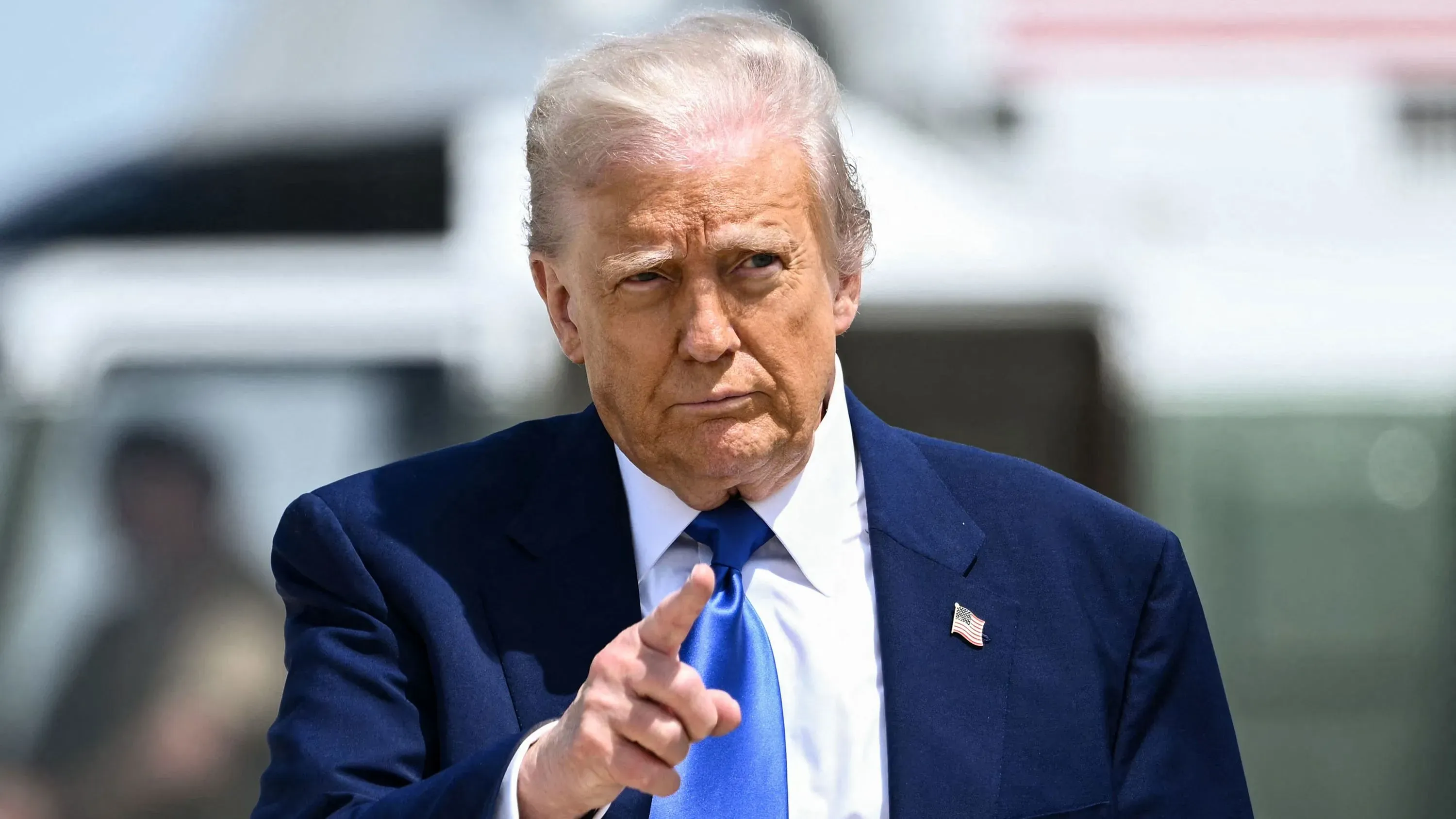 الرئيس الأمريكي السابق دونالد ترامب يشير بإصبعه، مع خلفية غير واضحة لطائرة، في سياق مناقشات حول استثماراته في العملات الرقمية.