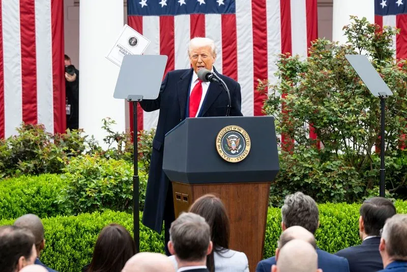 ترامب يتحدث في مؤتمر صحفي بالحديقة الجنوبية للبيت الأبيض، محاطًا بالأعلام الأمريكية، حيث يناقش تأثير الرسوم الجمركية على الاقتصاد.