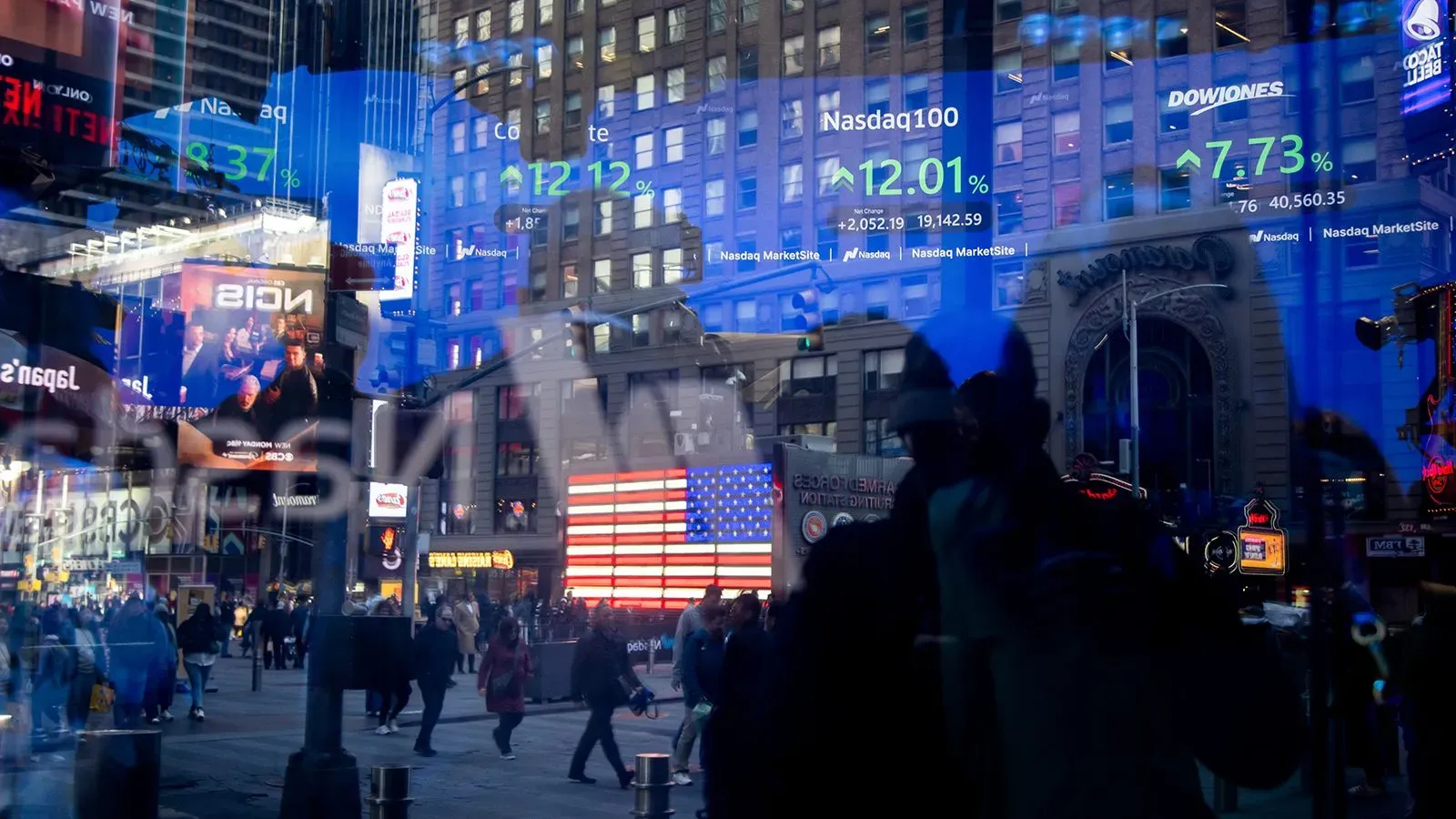 شاشة عرض في منطقة تايمز سكوير تظهر بيانات سوق الأسهم الأمريكية مع العلم الأمريكي في الخلفية، تعكس حالة الاقتصاد والتوترات التجارية.