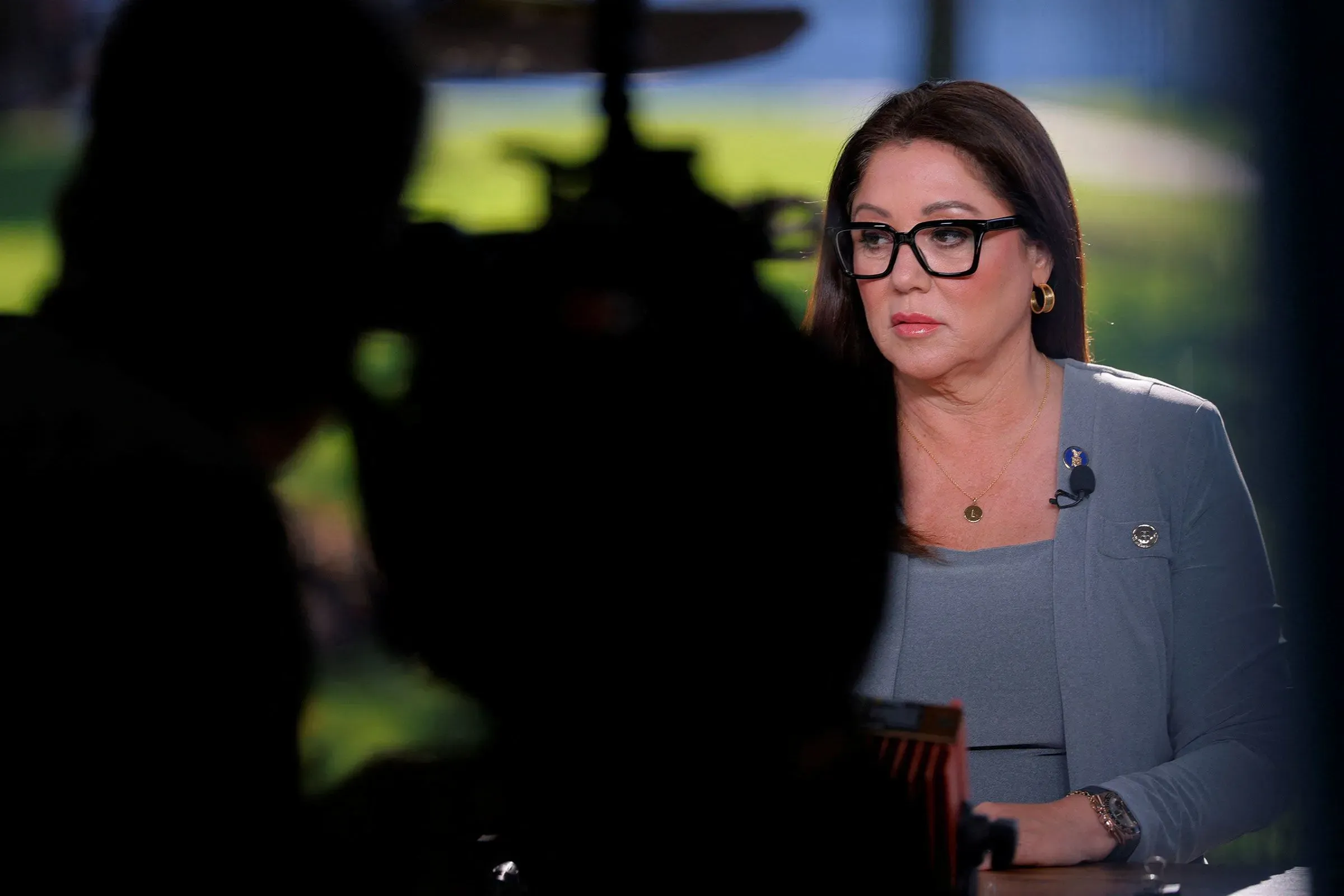 امرأة ترتدي نظارات وتظهر بملامح جادة خلال مقابلة، مع خلفية ضبابية. تعكس الصورة الأجواء السياسية المتوترة حول الاقتصاد.