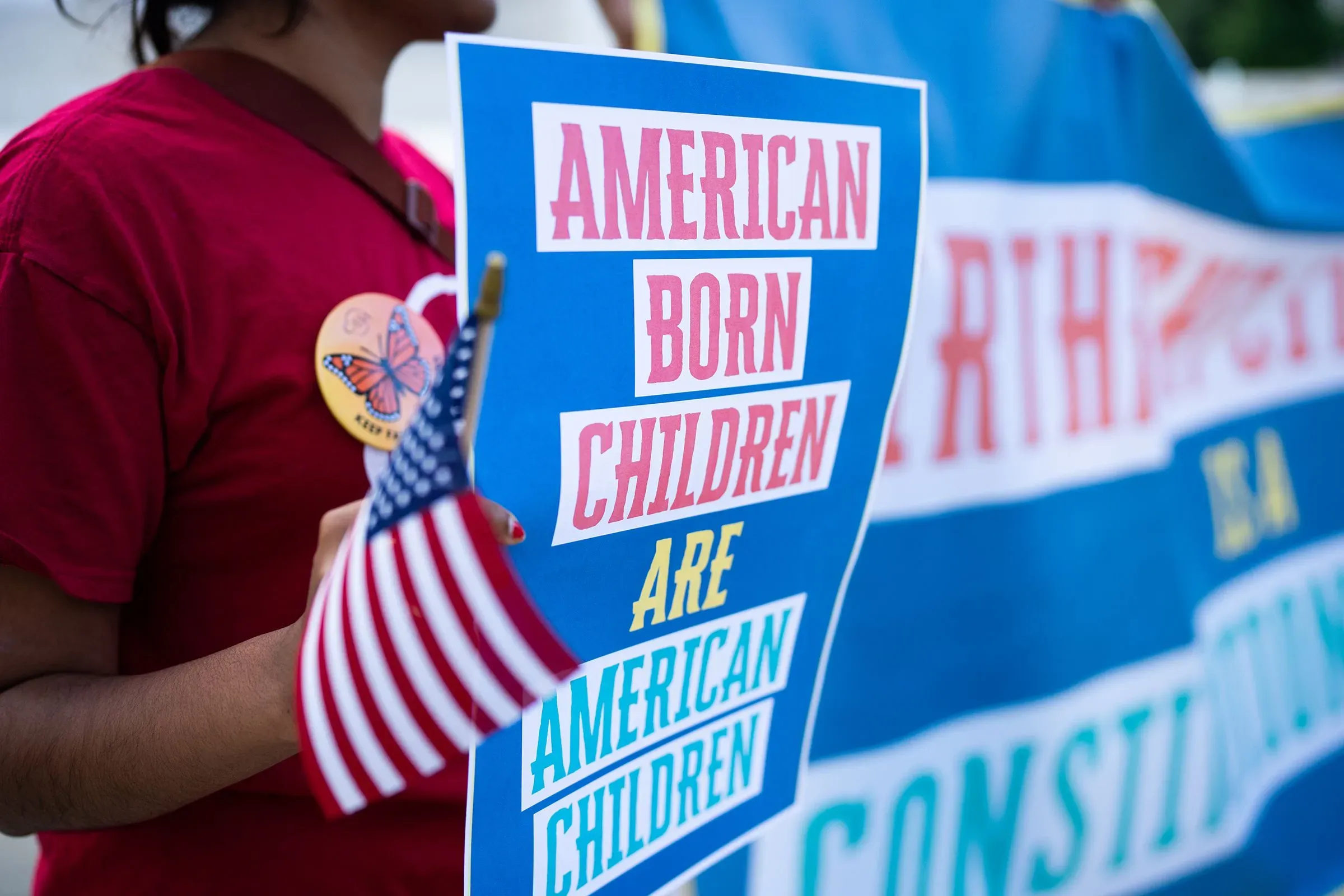 لافتة تحمل شعارات تدعم حق المواطنة بالميلاد للأطفال المولودين في الولايات المتحدة، مع علم أمريكي صغير.