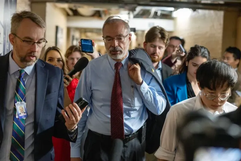 مجموعة من الأشخاص في مبنى الكابيتول هيل، يتحدثون ويستخدمون هواتفهم، وسط أجواء من التوتر السياسي حول مشروع قانون الميزانية.