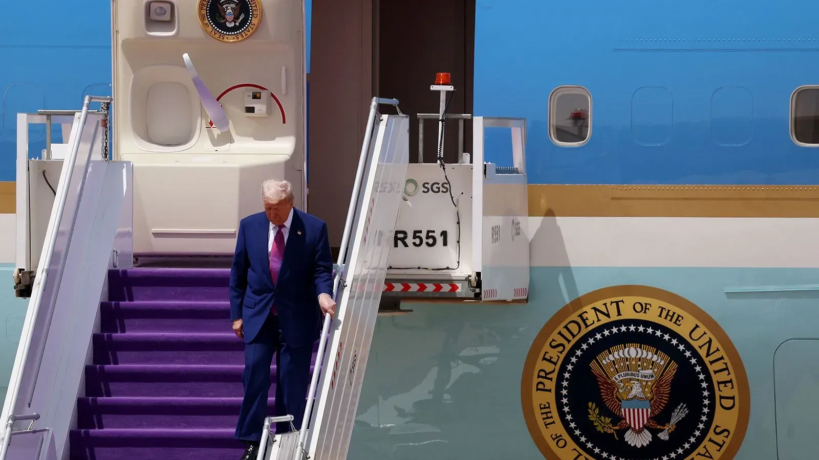 الرئيس الأمريكي دونالد ترامب ينزل من طائرته الرئاسية، محاطًا بأجواء رسمية، وسط تساؤلات حول هدية محتملة من قطر.