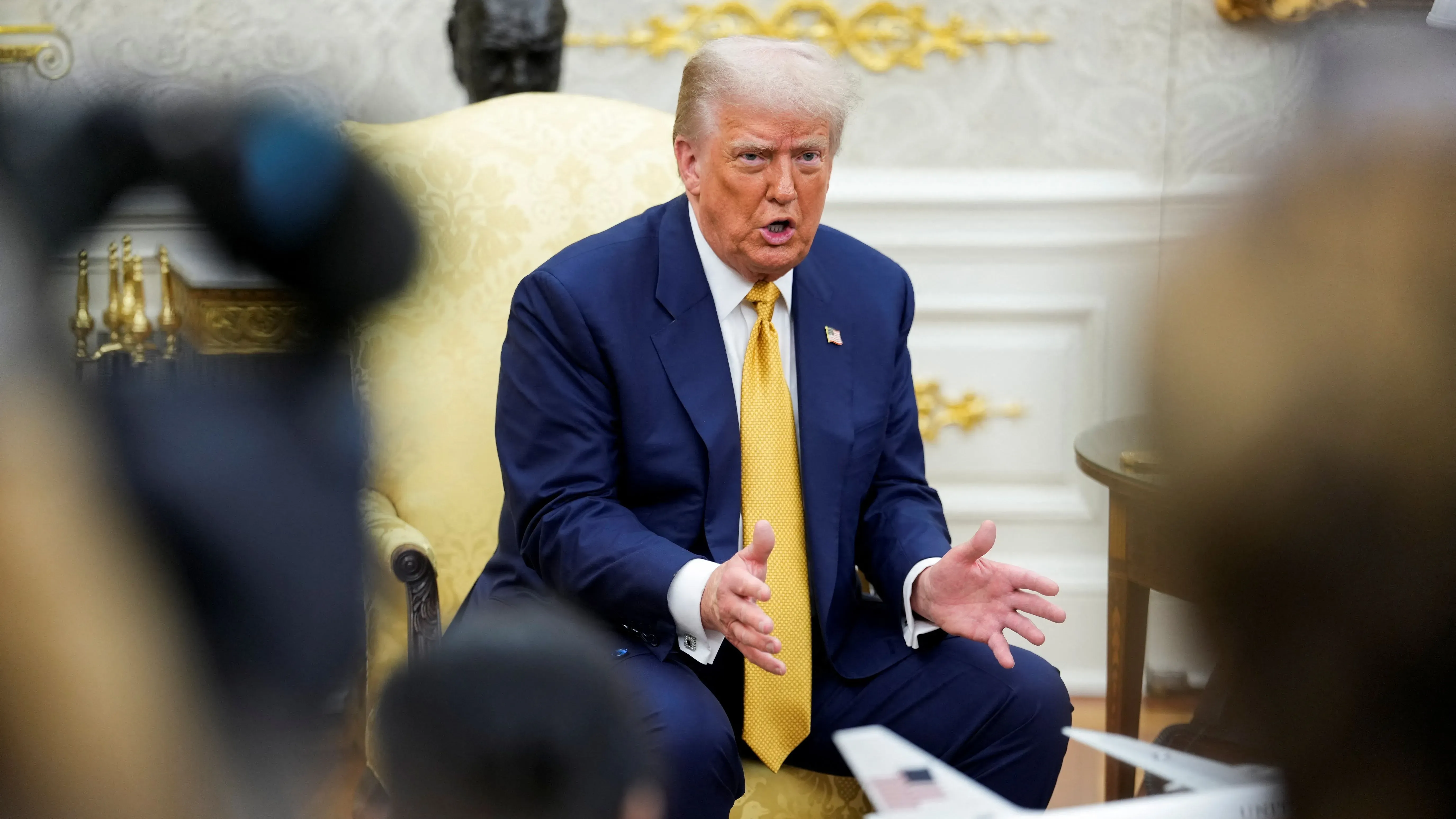 ترامب يتحدث بجدية أثناء جلوسه في المكتب البيضاوي، مع التركيز على قضايا تتعلق بأوباما وروسيا، وسط كاميرات الإعلام.