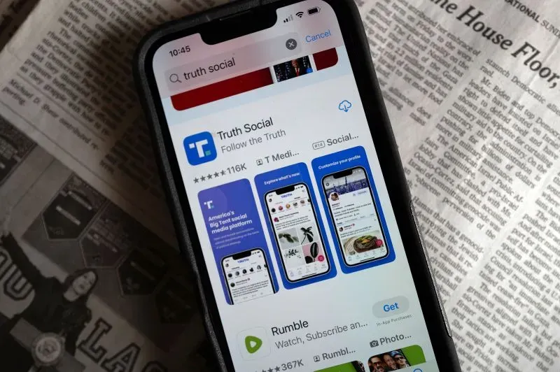 واجهة تطبيق "Truth Social" على هاتف ذكي، مع خلفية لصحيفة، تعكس الجدل حول برامج التنوع والشمول في إدارة ترامب.
