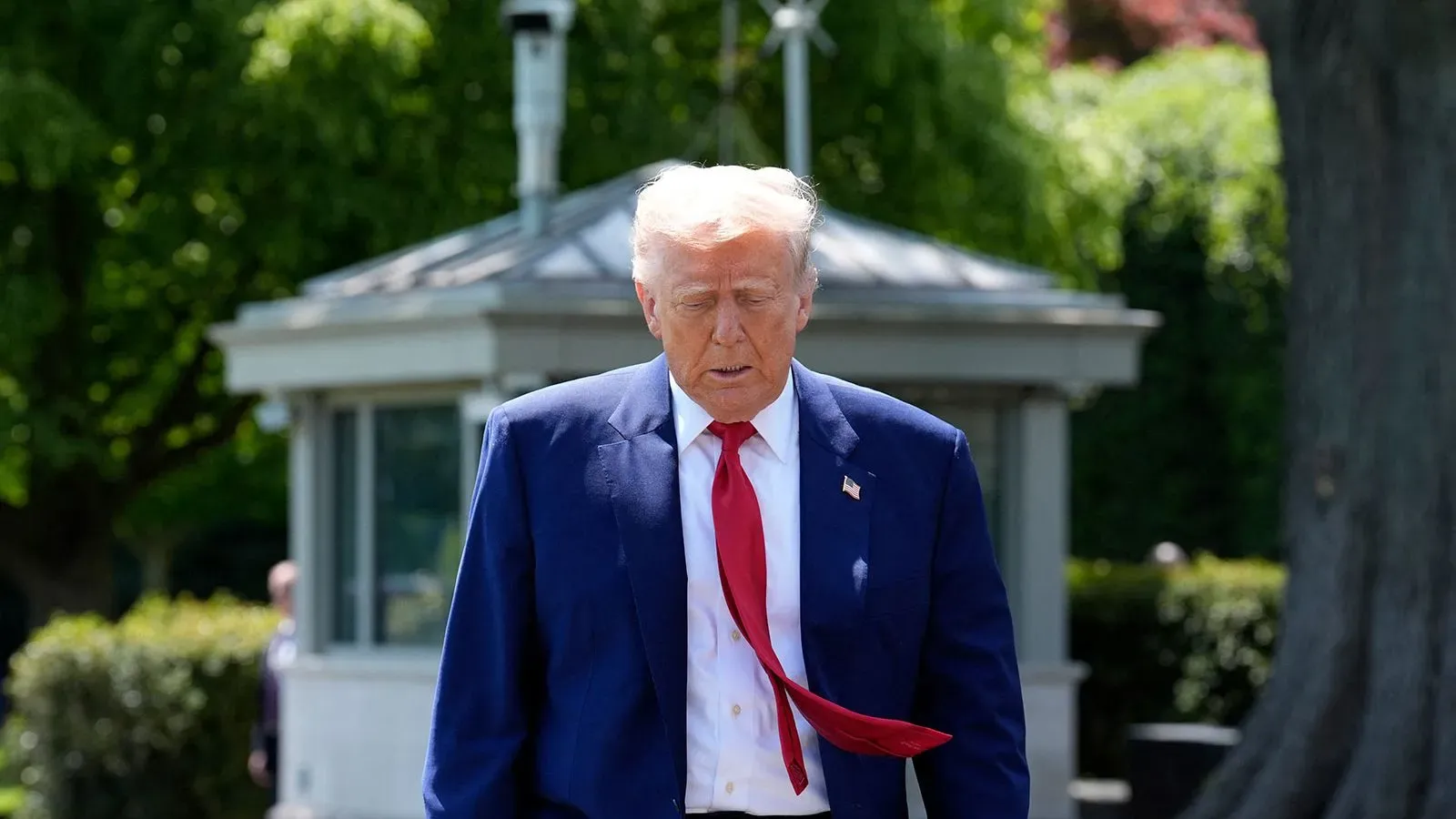 ترامب يسير خارج البيت الأبيض، مرتديًا بدلة زرقاء وربطة عنق حمراء، مع تعبير جاد، في سياق مناقشة الرسوم الجمركية على الأفلام.
