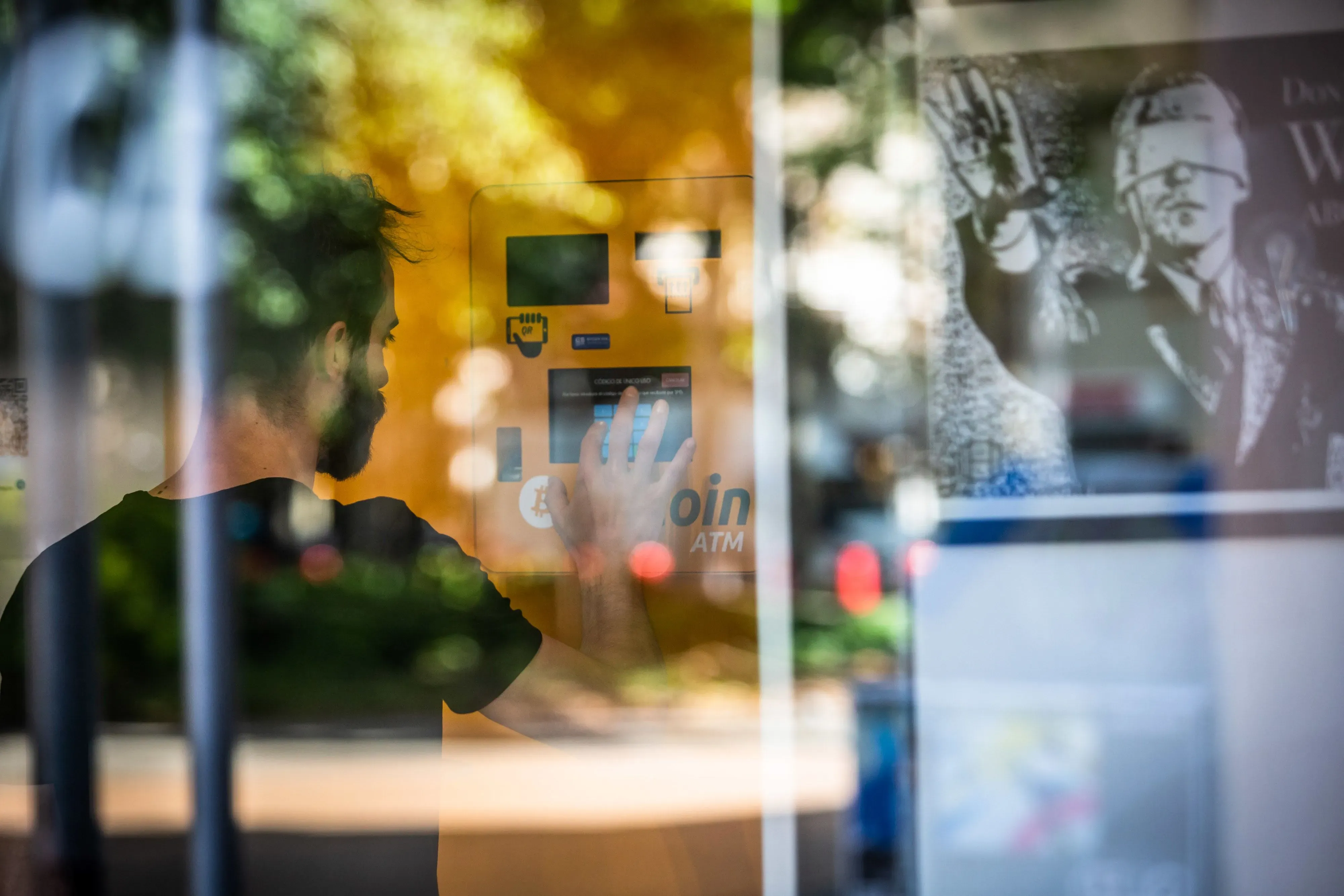 رجل يستخدم ماكينة صراف آلي للعملات الرقمية، مع وجود صورة خلفية توضح تفاصيل العملات الرقمية. تعكس الصورة تزايد الاهتمام بالبيتكوين والإيثر.
