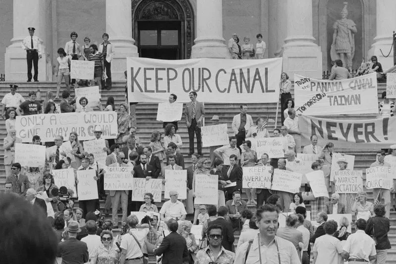 مظاهرة كبيرة أمام مبنى حكومي، حيث يحمل المتظاهرون لافتات تطالب بالحفاظ على قناة بنما، مع شعارات تعبر عن معارضتهم للتسليم.