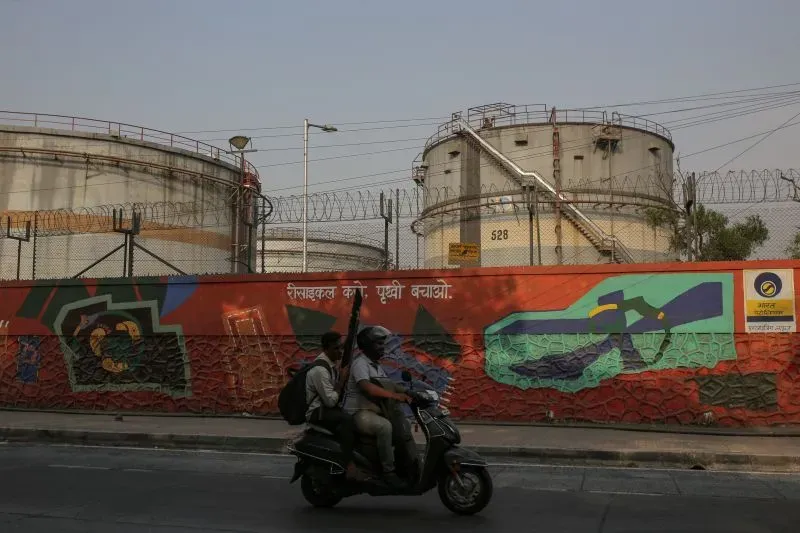 صورة تظهر خزانات نفط كبيرة خلف سياج شائك، مع جدار مزين برسومات جرافيتي، تعكس أهمية النفط في السياق الجيوسياسي.