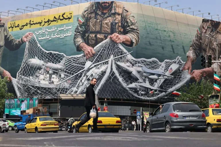ملصق كبير يظهر جندياً إيرانياً يحمل شبكة تحتوي على طائرات مسيرة، مع سيارات تسير في الشارع. يعكس التوترات في مضيق هرمز.
