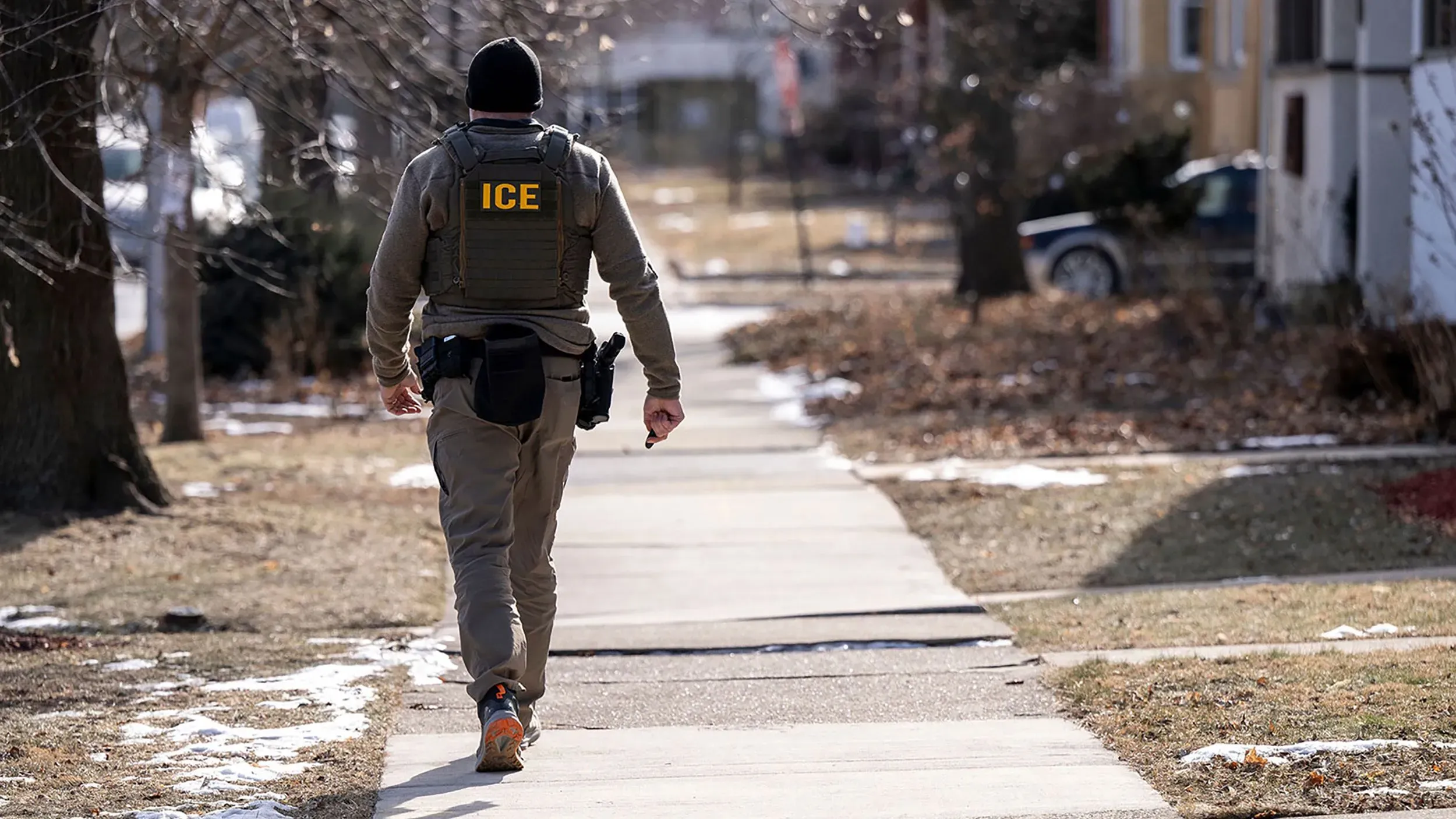 موظف من إدارة الهجرة والجمارك (ICE) يسير على الرصيف، مما يعكس التوترات حول سياسات الهجرة في عهد ترامب.