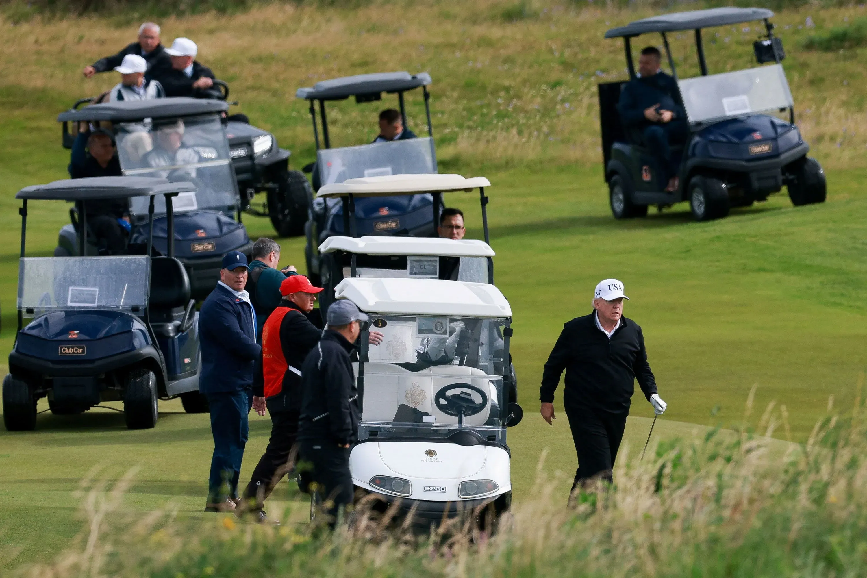 ترامب يتجول في ملعب غولف في اسكتلندا، محاطًا بعدد من العربات، بينما يستعد لزيارة ممتلكاته للغولف ويعقد اجتماعات عمل.