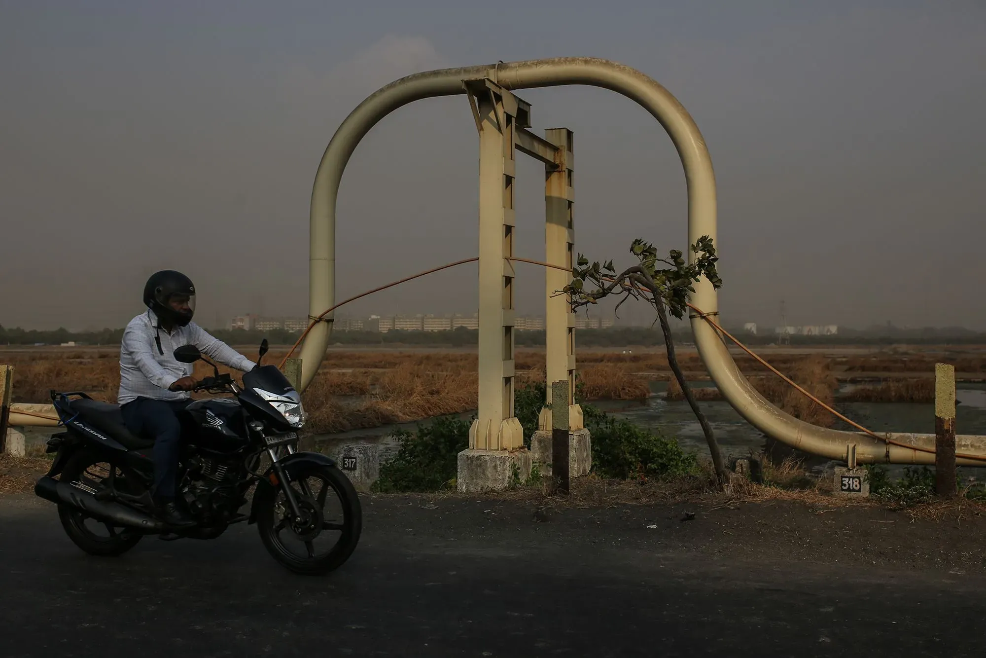 رجل يرتدي خوذة يقود دراجة نارية بجوار أنابيب نفطية في منطقة جافة، مما يعكس تأثيرات الصراع في أوكرانيا على سوق الطاقة العالمي.