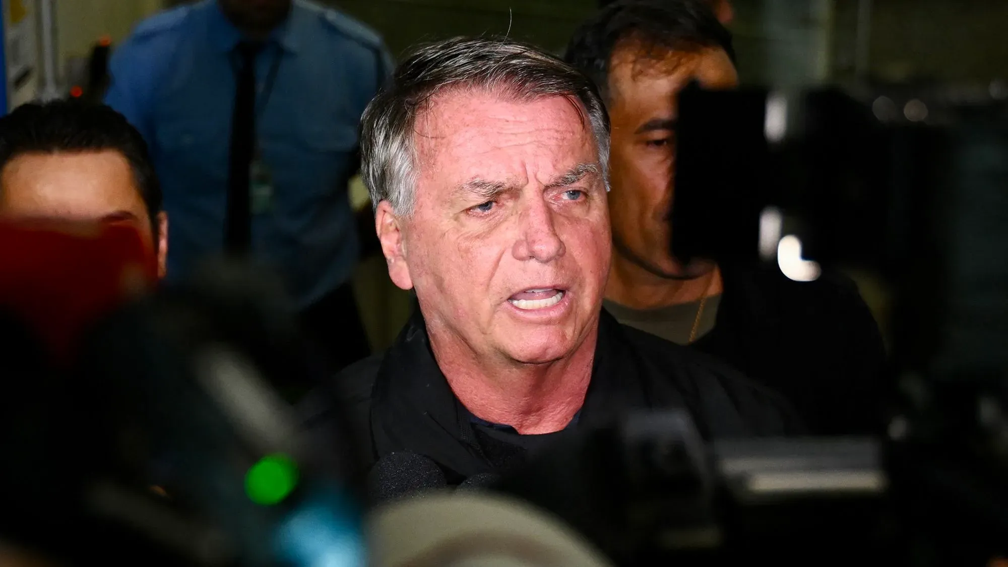 الرئيس البرازيلي السابق جايير بولسونارو يتحدث للصحافة وسط مجموعة من الصحفيين، في سياق قضية قانونية تتعلق بحرية التعبير.