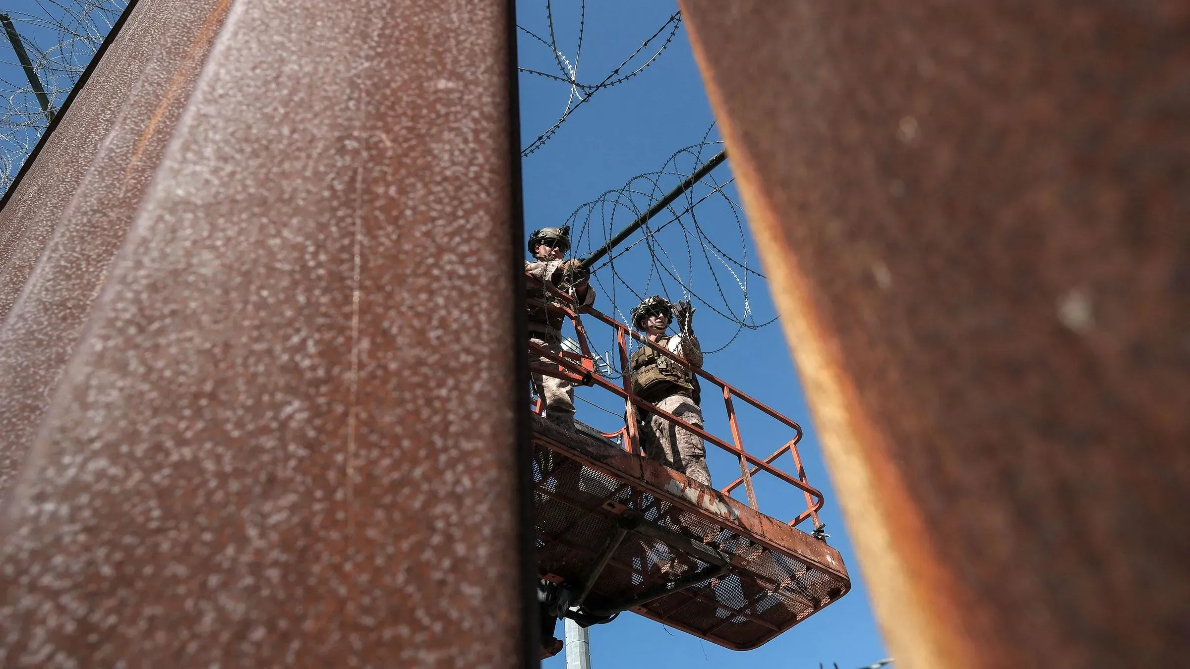 جنود أمريكيون يقومون بمراقبة الحدود من منصة مرتفعة، حيث يظهر السلك الشائك على السياج الفاصل بين الولايات المتحدة والمكسيك.