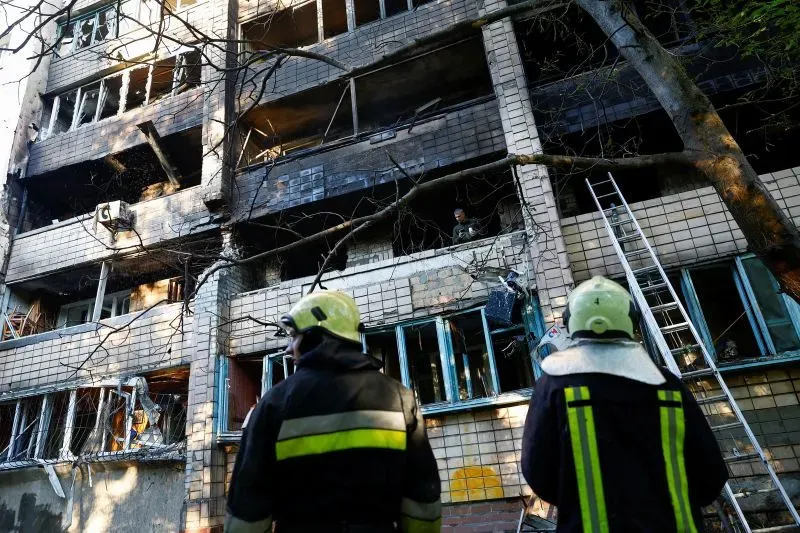 رجال إطفاء يتابعون الأضرار في مبنى سكني متضرر من القصف في أوكرانيا، مع ظهور آثار الدمار على الواجهة والنوافذ المحطمة.