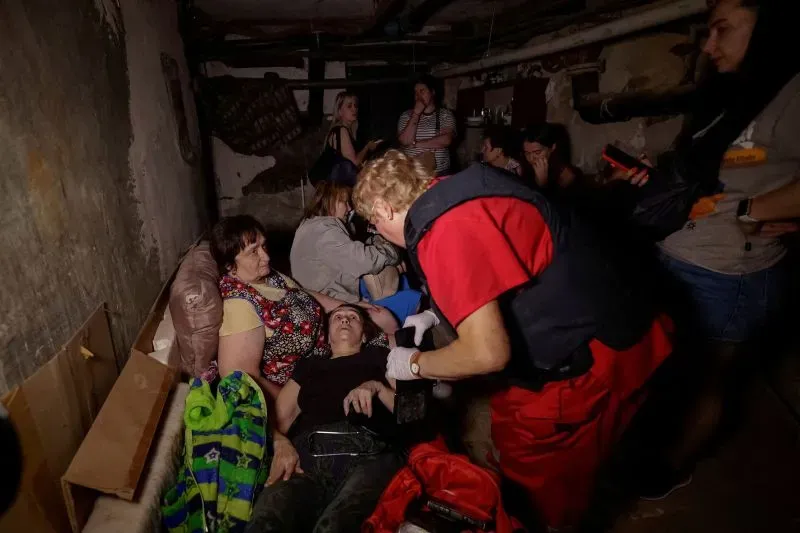 نساء وأطفال في ملجأ تحت الأرض أثناء الهجمات في أوكرانيا، مع مسعف يقدم المساعدة لامرأة مصابة.