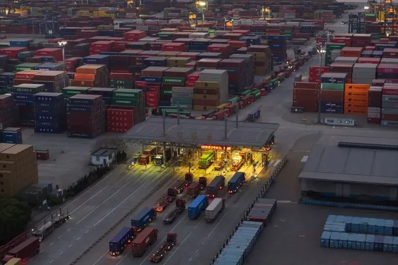 ازدحام مروري في ميناء شحن مزدحم، مع صفوف من الحاويات الملونة والشاحنات، مما يعكس التوترات التجارية بين الولايات المتحدة والصين.