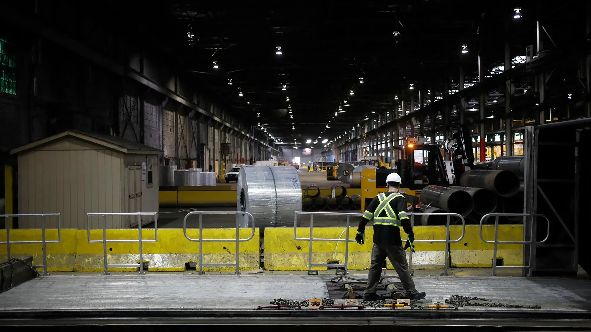 عامل يرتدي خوذة وملابس واقية داخل مصنع، محاط بأدوات وآلات التصنيع، في سياق جهود إعادة التصنيع الأمريكية.