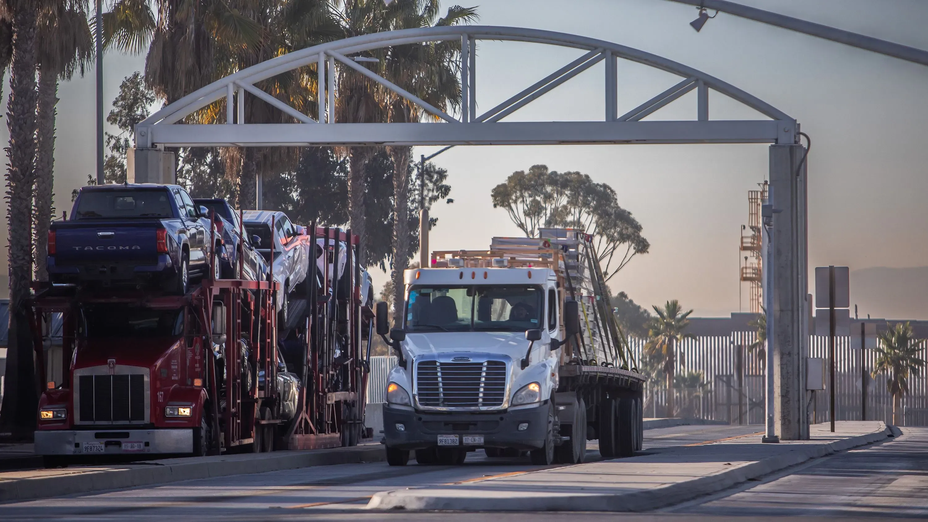 شاحنات نقل تحمل سيارات تعبر نقطة حدودية، تعكس تأثير التعريفات الجمركية على التجارة بين الولايات المتحدة وكندا والمكسيك.