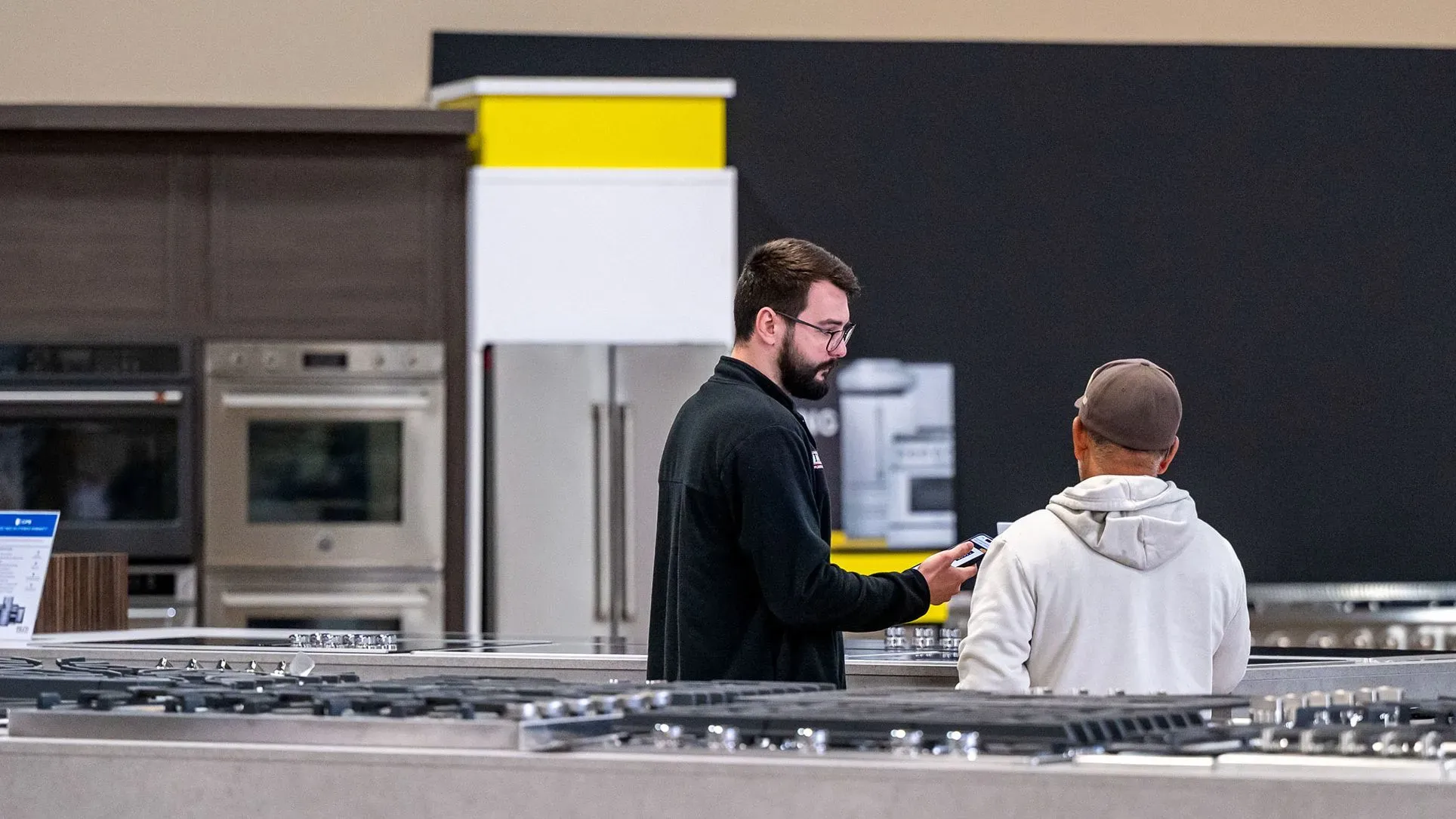 مشتريَان يتحدثان في متجر للأجهزة المنزلية، حيث يناقشان خيارات الشراء وسط تغييرات في أنماط الإنفاق بسبب التضخم.