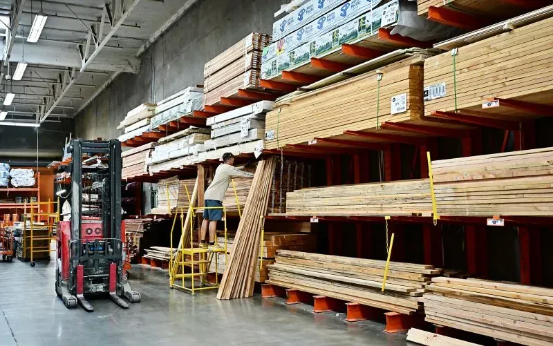 عامل يقوم بتنظيم الخشب في مستودع مواد البناء، مما يعكس تأثير زيادة تكاليف المواد على صناعة البناء في الولايات المتحدة.