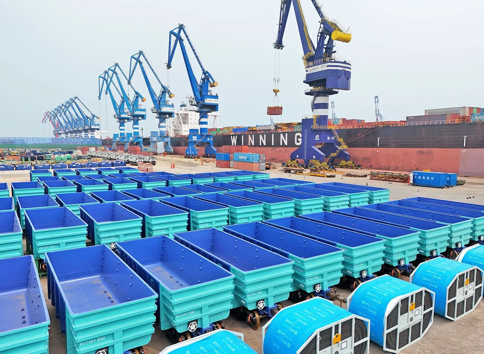 مستودع شحن يحتوي على حاويات زرقاء وشاحنات، مع رافعات في الخلفية، يعكس تأثير التعريفات الجمركية على التجارة الأفريقية.