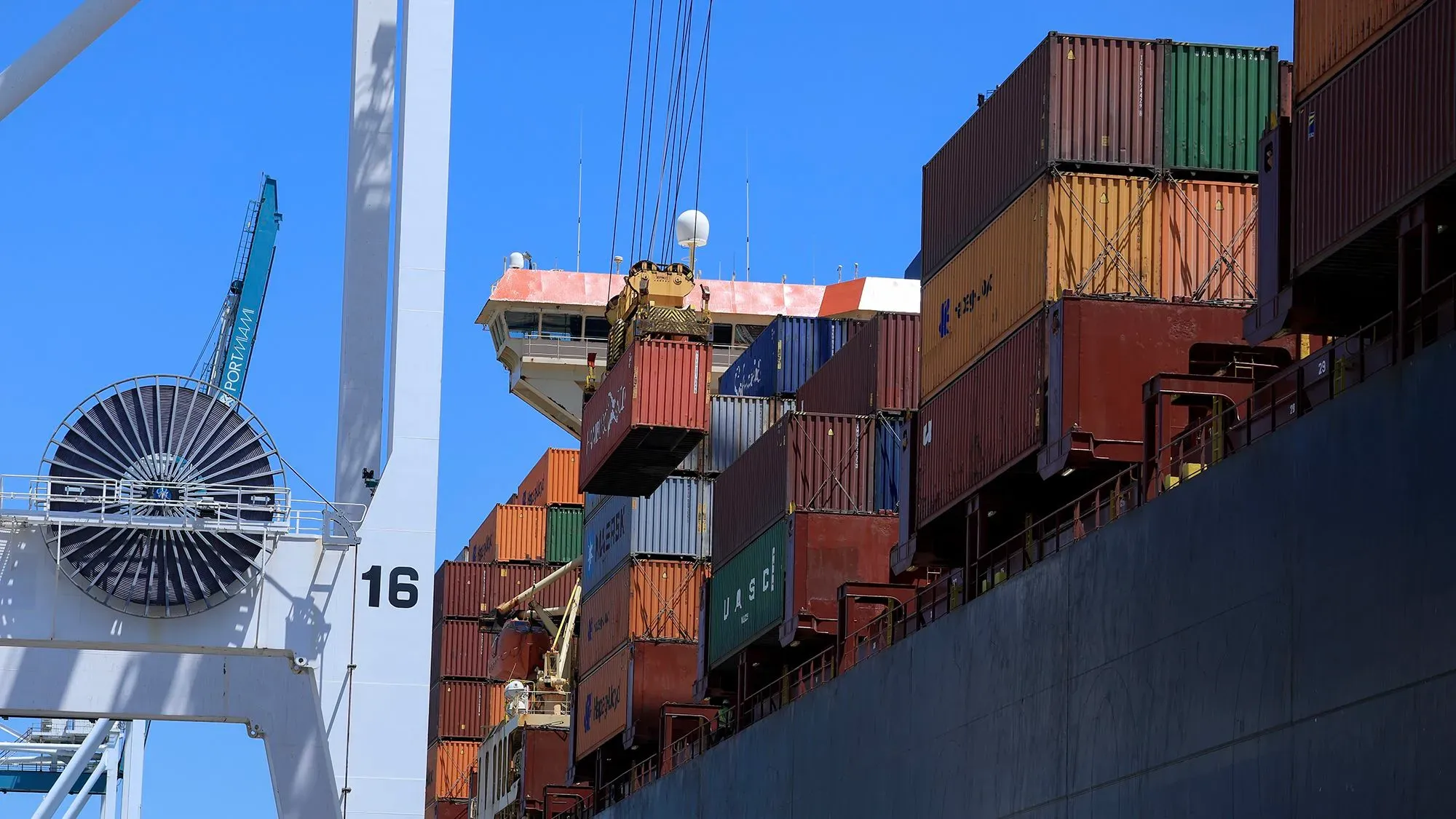 حاويات شحن ملونة متراكمة على سفينة في ميناء، مع وجود رافعة تحميل في الخلفية، تعكس حركة التجارة العالمية.