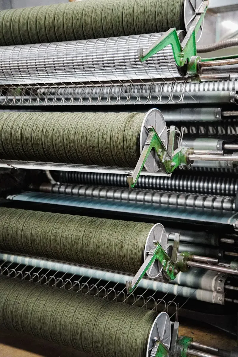 خيوط صوفية خضراء على آلات مطحنة فاريبولت، تمثل مراحل إنتاج البطانيات في مصنع تاريخي بجنوب مينيسوتا.