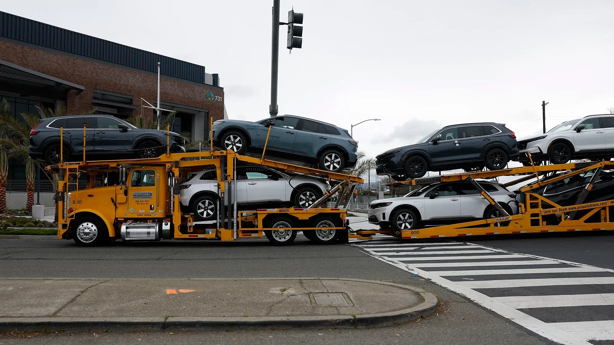 شاحنة نقل سيارات تحمل عدة سيارات جديدة، مع التركيز على تأثير التعريفات الجمركية على تكاليف السيارات وقطع الغيار في الولايات المتحدة.