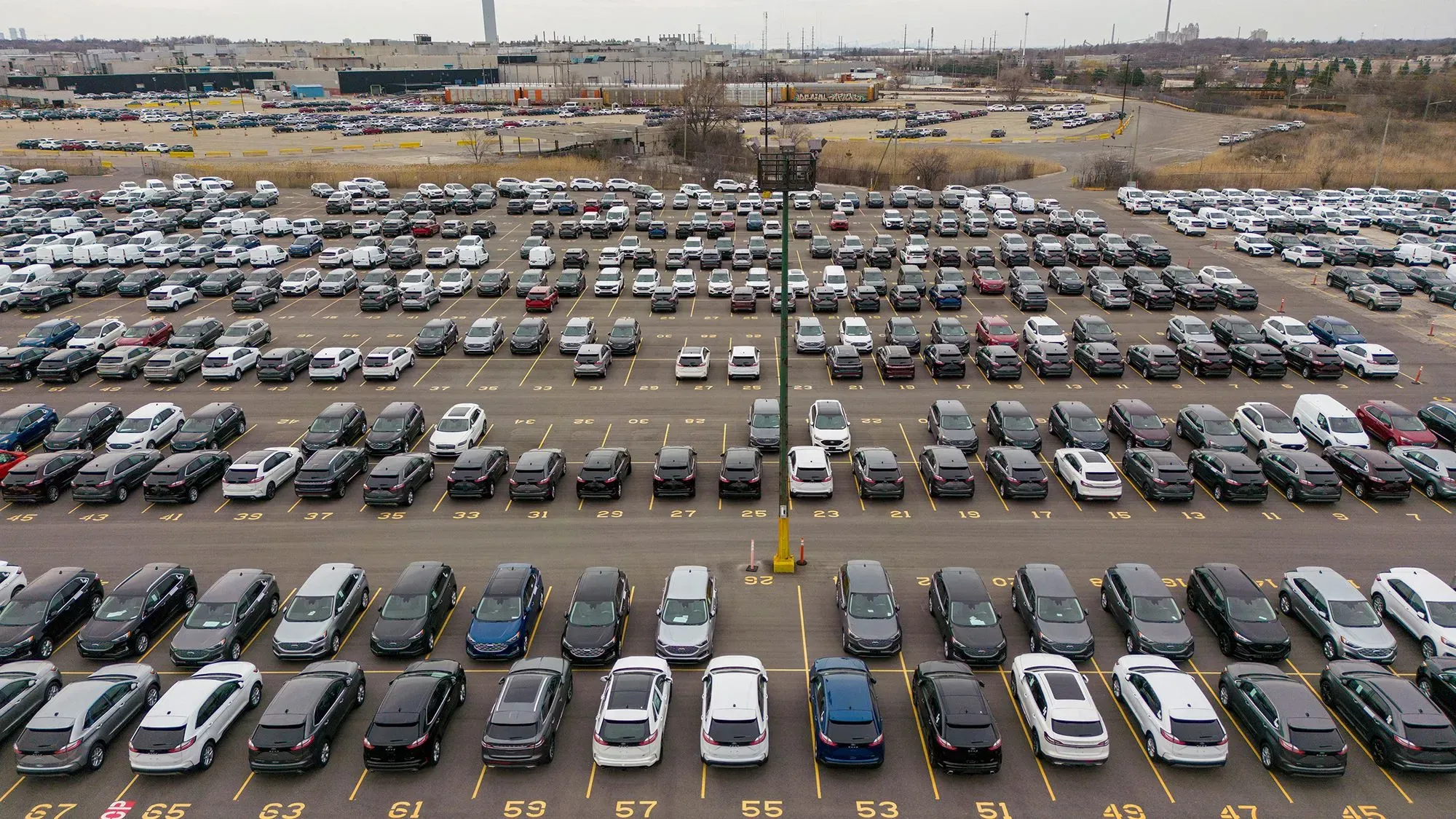 صورة لصفوف من السيارات المتوقفة في موقف سيارات واسع، تُظهر تأثير التوترات التجارية على صناعة السيارات.